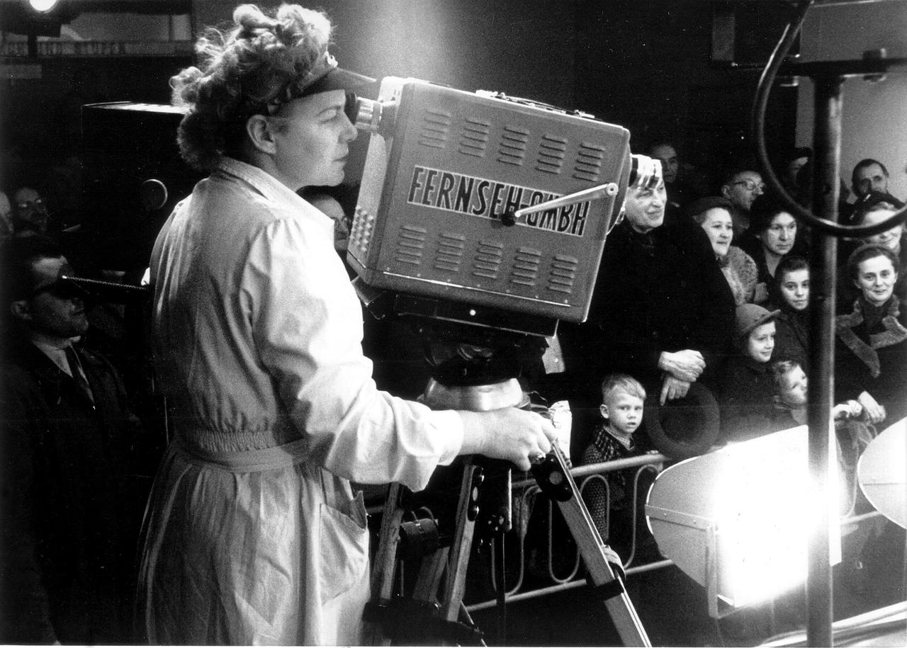 Eine Frau bedient 1954 eine große Fernsehkamera des Österreichischen Rundfunks vor einer Menschenmenge.