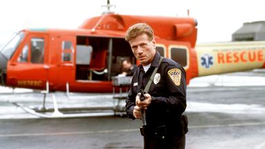 Quentin Darby (Jürgen Prochnow) steht mit einer Waffe neben einem kleinen Flugzeug