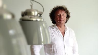 Ein Mann mit weißem Hemd und grauen lockigen Haaren.