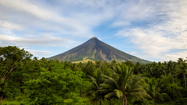 Perfekt geformter Kegel des Mayon-Vulkans auf Luzon, umgeben von dichter tropischer Vegetation unter blauem Himmel.