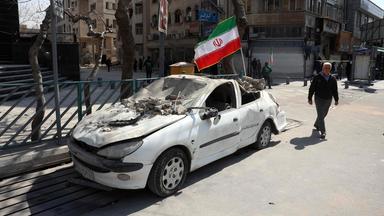 Mann läuft an einem von US-Angriff zerstörten Auto in Teheran vorbei.