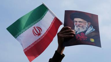 Eine Hand hält eine iranische Flagge und ein Bild vom getöteten iranischen Führer Ajatollah Ali Chamenei hoch.