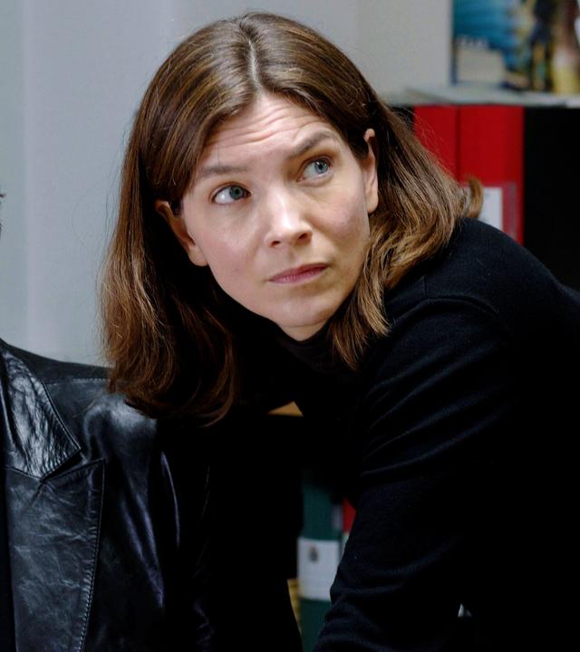 Eine Frau und ein Mann mittleren Alters schauen beide in dieselbe Richtung. Beide sind schwarz gekleidet.