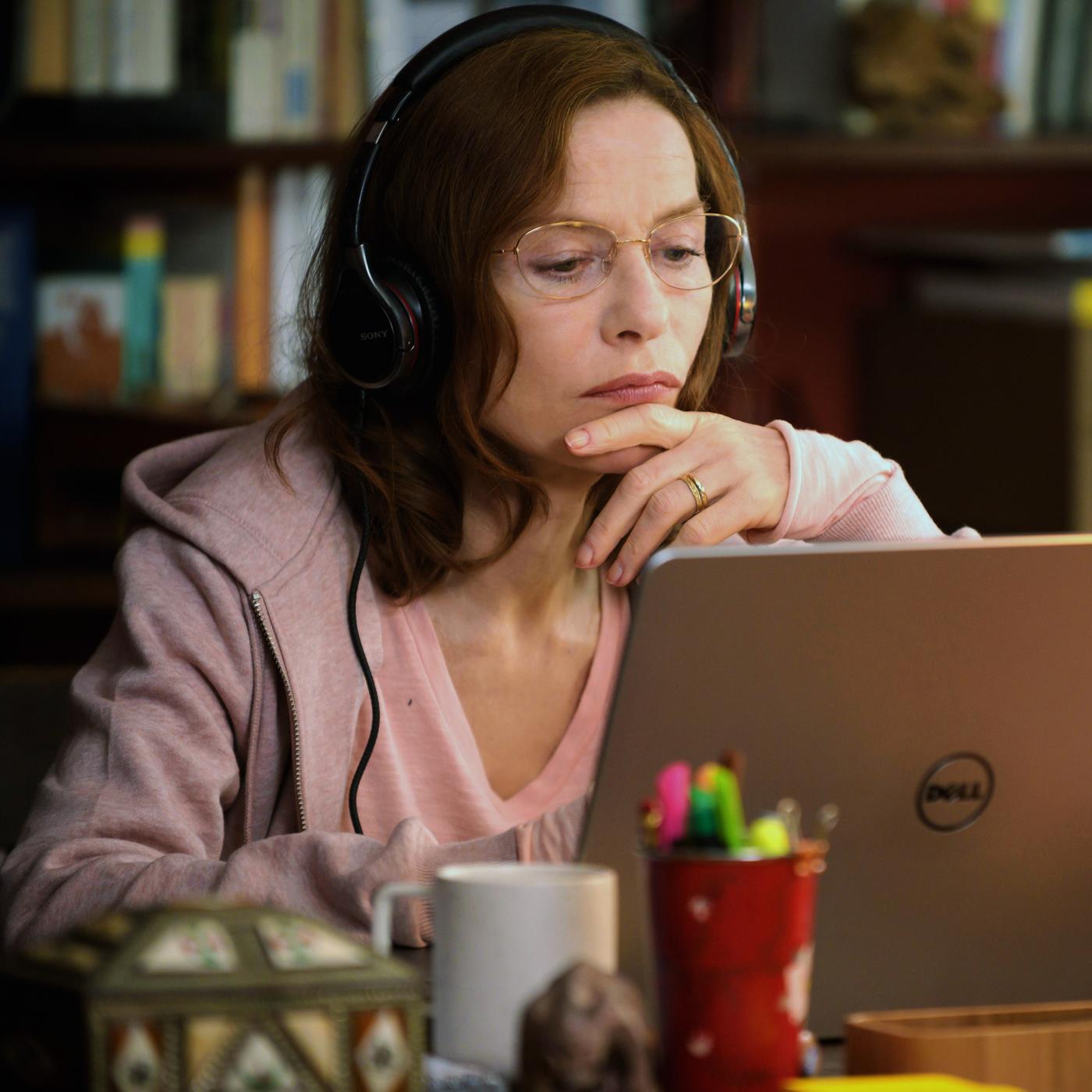 Eine Frau mit langen Haaren und Brille sitzt vor einem aufgeklappten Laptop.
