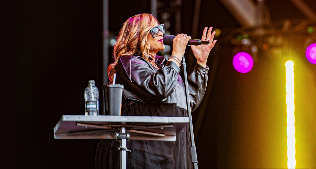 Gabrielle im schwarzen Ledermantel und Sonnenbrille auf der Bühne. In der Hand hält sie ein Mikrofon.