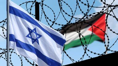 Die Flagge Israels und die palästinensische Flagge wehen im Wind, zwischen ihnen Stacheldraht.