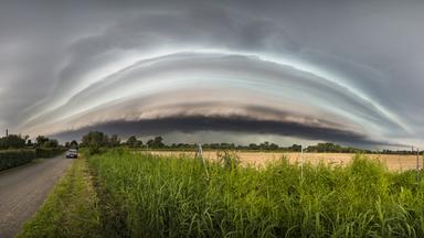 Am Himmel braut sich ein Gewitter zusammen. Ein Auto fährt an einem Feld entlang.