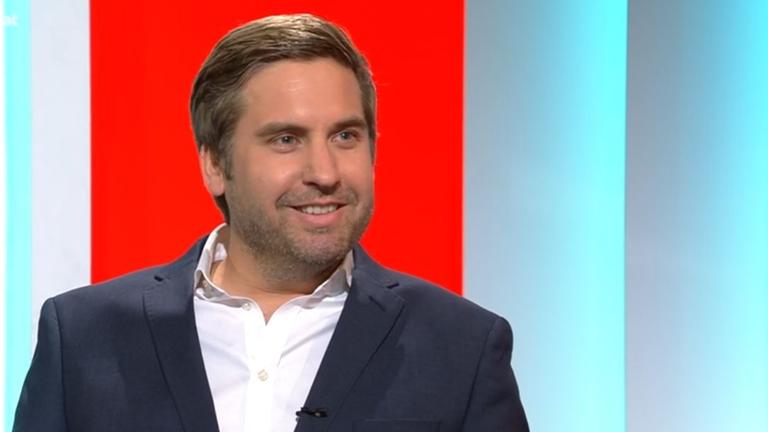 Braunhaariger Mann vor rot-blauem Studio-Hintergrund.