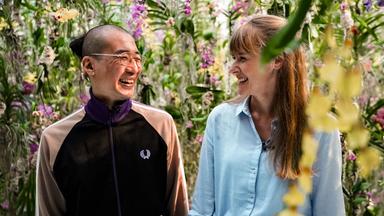 Eine Mann und eine Frau lachen sich an. Sie sind umgeben von Blumen.