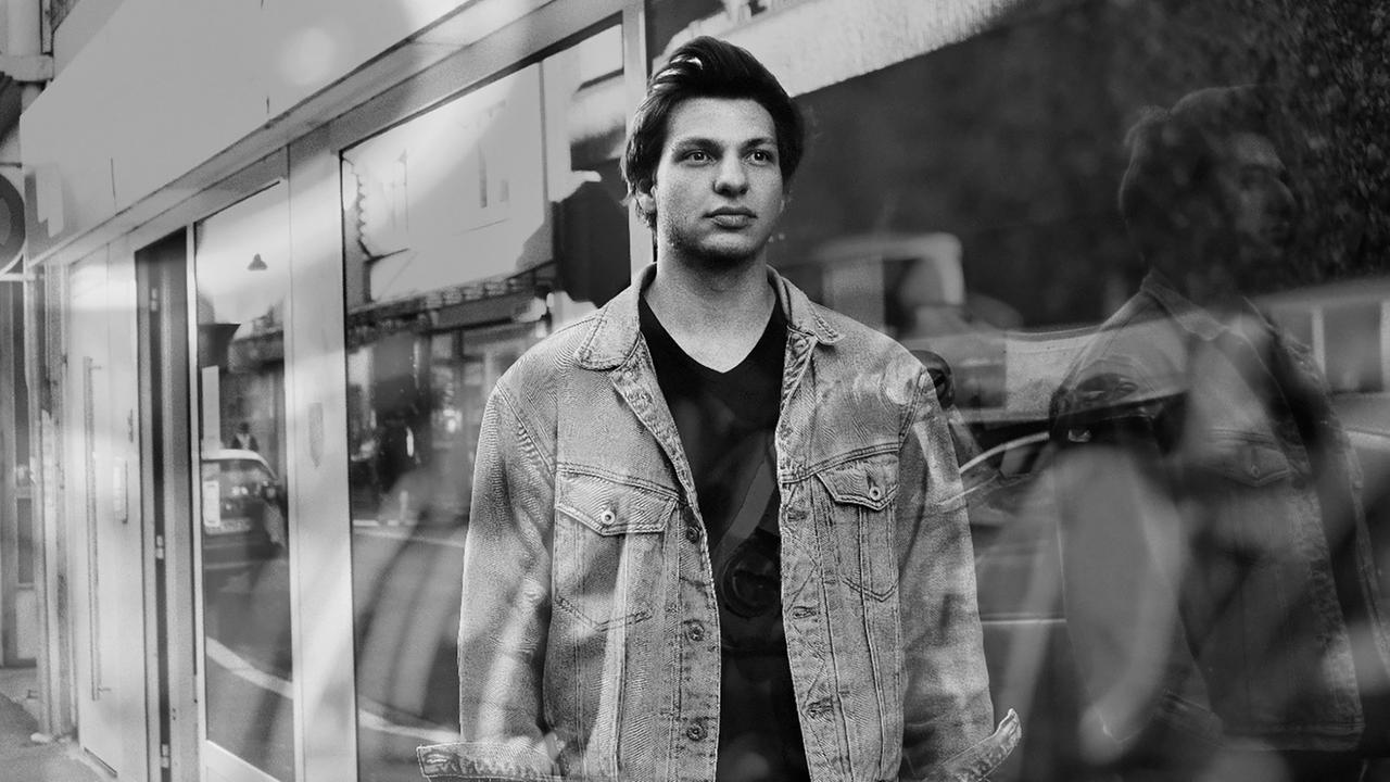 Das schwarz-weiß Foto eines jungen Mannes, der vor einem Schaufenster steht, in dem er sich spiegelt.