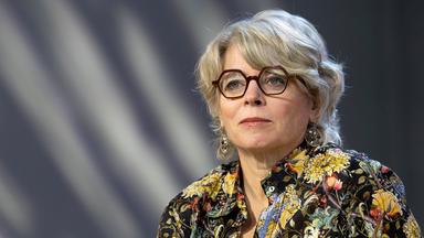 Frau mit Brille und grauen halblangen Haaren schaut an der Kamera vorbei