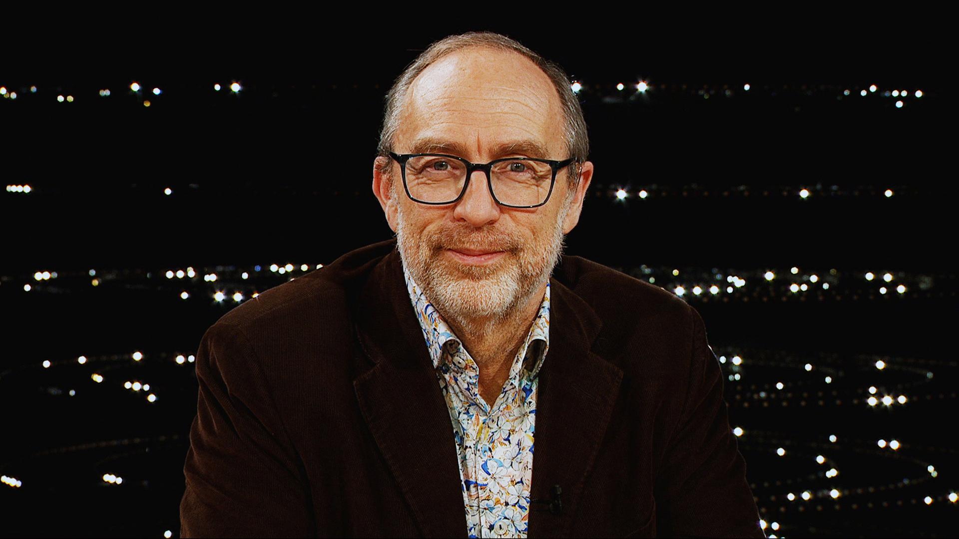 Ein Mann mit Brille schaut vor dunklem Hintergrund in die Kamera