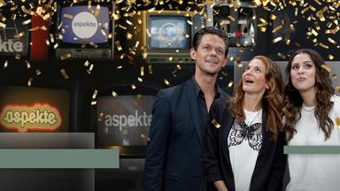 Jo Schück, Katty Salié und Salwa Houmsi feiern 60 Jahre aspekte. Neben den drei ModeratorInnen sind Bildschirme mit aspekte-Logos der Vergangenheit zu sehen, von der Decke fällt Konfetti 