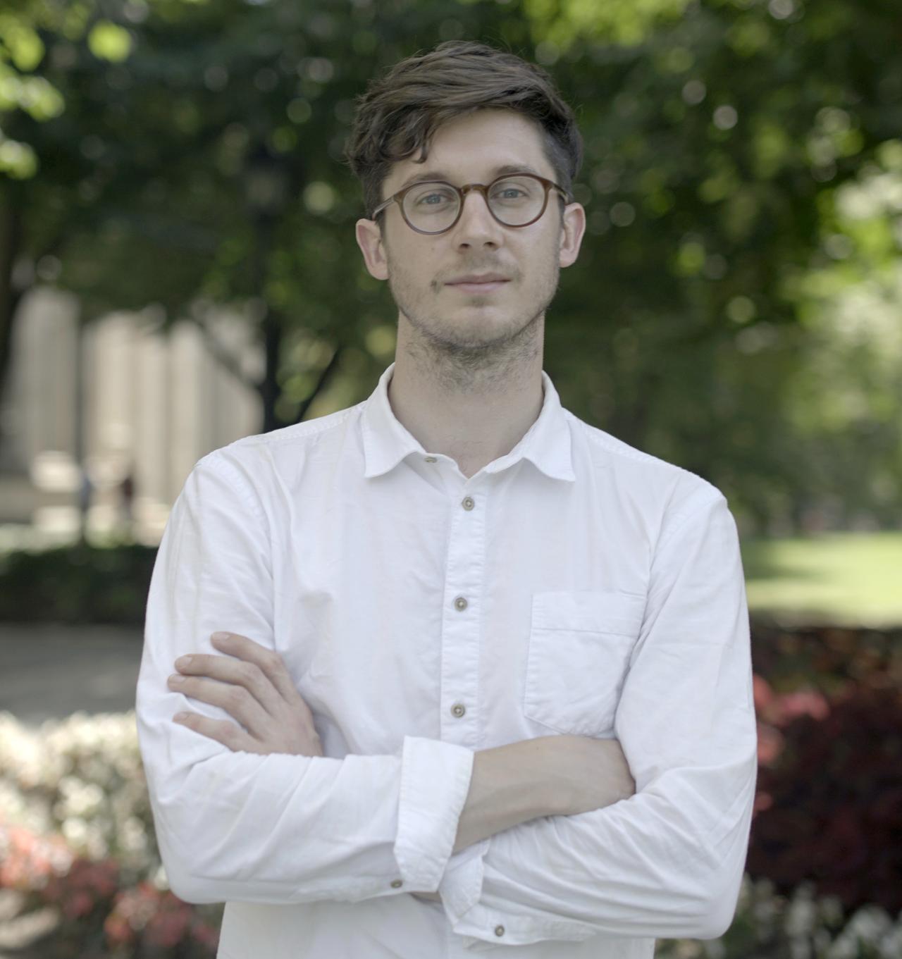 Porträtaufnahme von Florian Baron, der ein weißes Oberhemd trägt und mit verschränkten Armen in die Kamera schaut.