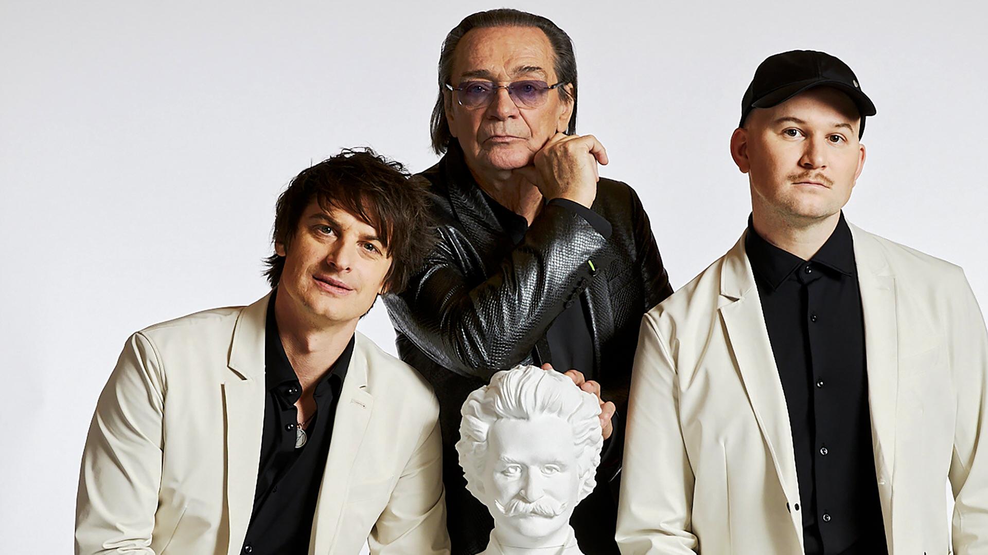 Drei Männer sthen um eine weisse Büste von Johann Strauss