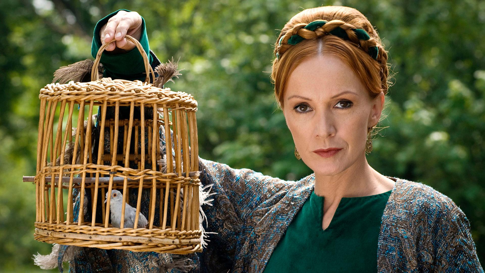 Eine Frau hält einen Korbkäfig mit einer Nachtigall hoch.