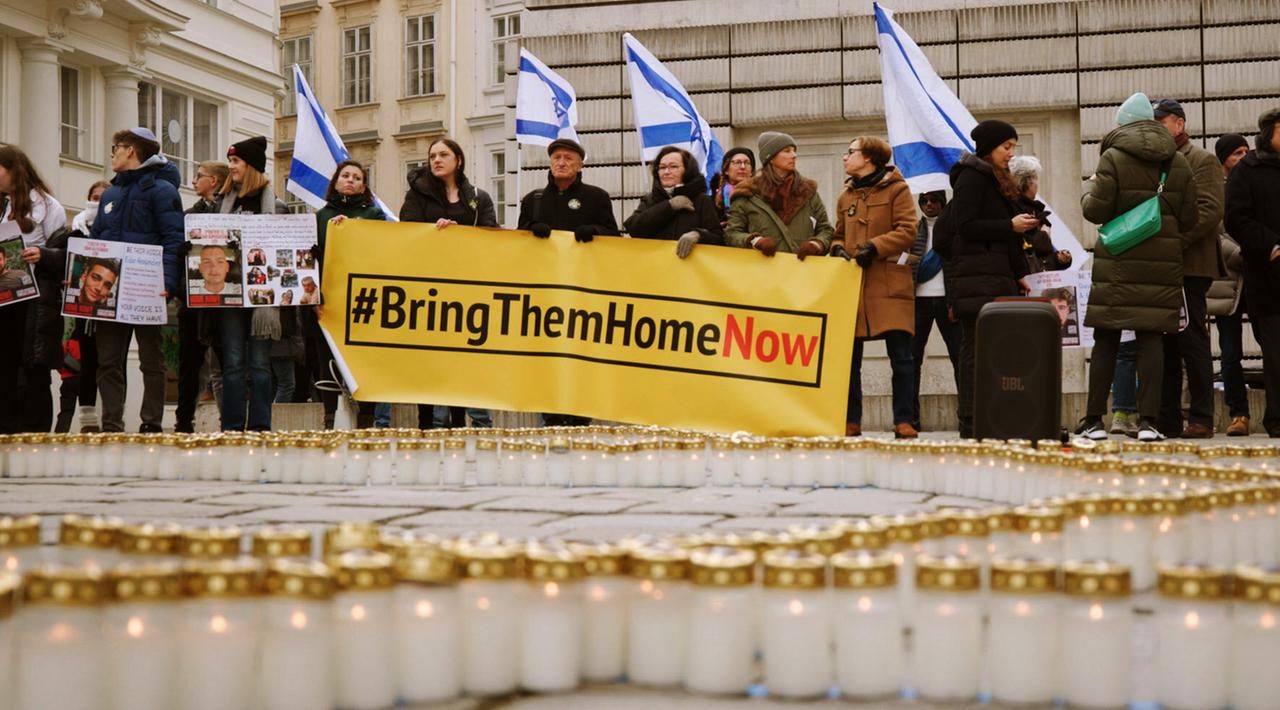 Viele Menschen halten ein langes, gelbes Transparent mit der Aufschrift "Bring them home now"