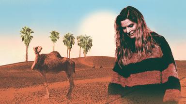 Ein Porträt von Eva Briegel von Juli vor der Wüste. Sie blickt nach unten. Neben ihr ist ein Kamel zu sehen.