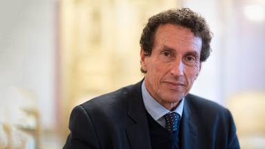 Porträtfoto eines Mannes mit kurzen gelockten Haaren in Anzug mit Krawatte.