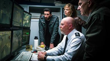 Assad (Fares Fares), Lisa (Signe Anastassia Mannov) und das Einsatzteam (Darsteller unbekannt) stehen vor Monitoren und starren gebannt darauf.