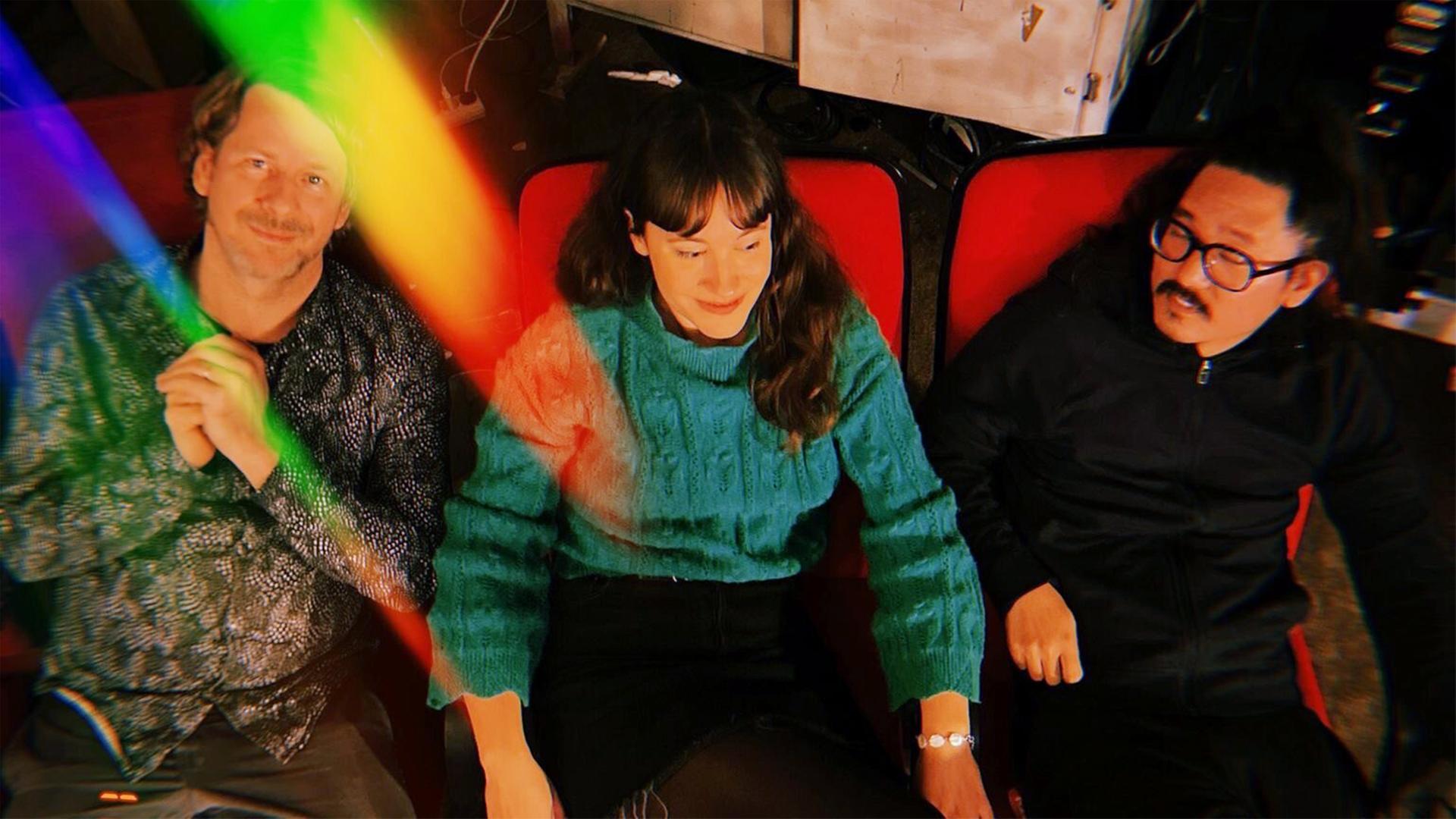 Drei Musiker*innen sitzen nebeneinander auf roten Stühlen mit farbigem Licht bei JazzBaltica 2026