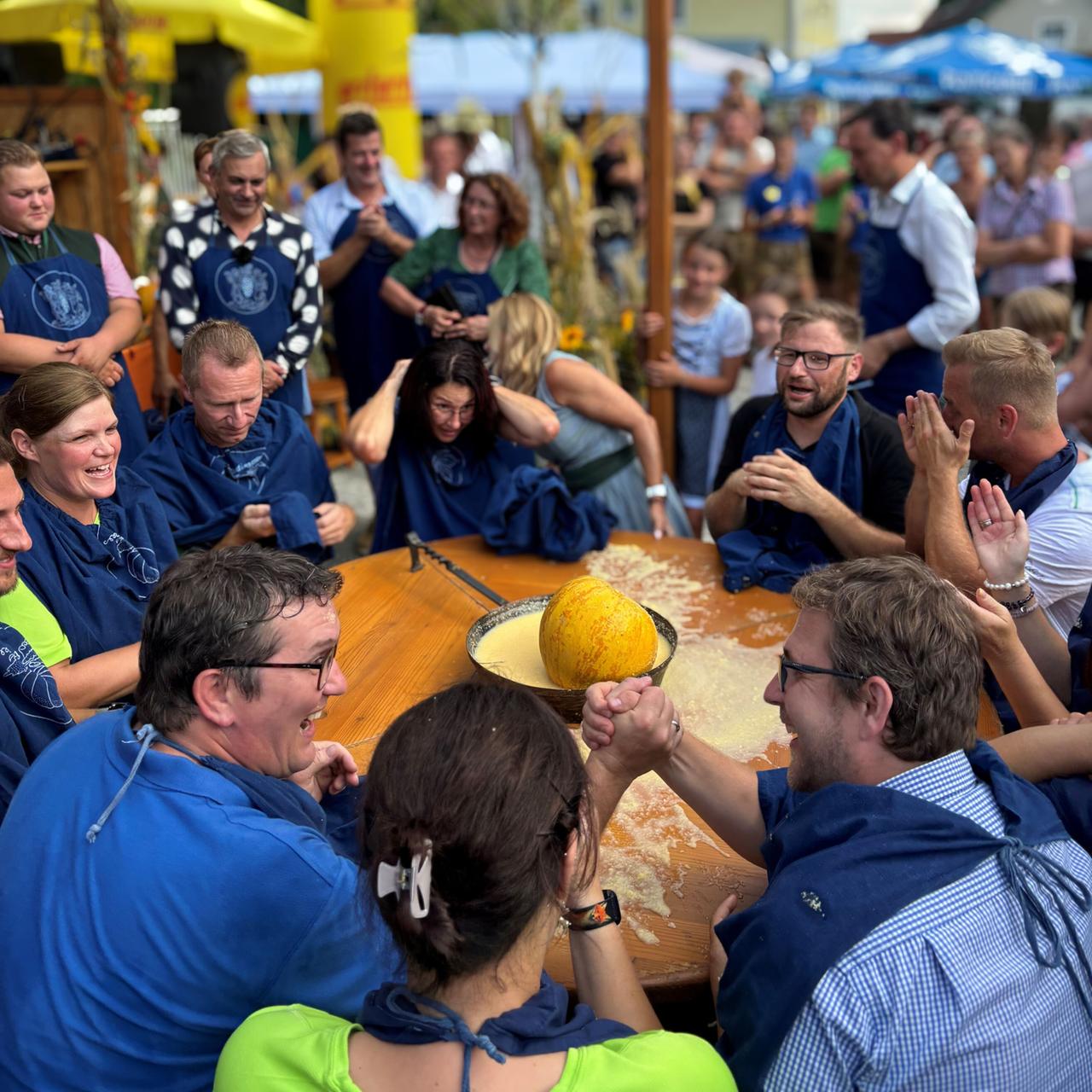 Menschen in traditioneller Kleidung und Schürzen bei einem herbstlichen Fest in Österreich, umgeben von Zuschauern und dekorativen Elementen.