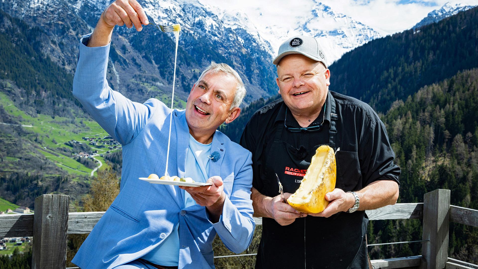Zwei Männer mit Käse vor einem Alpenpanorama