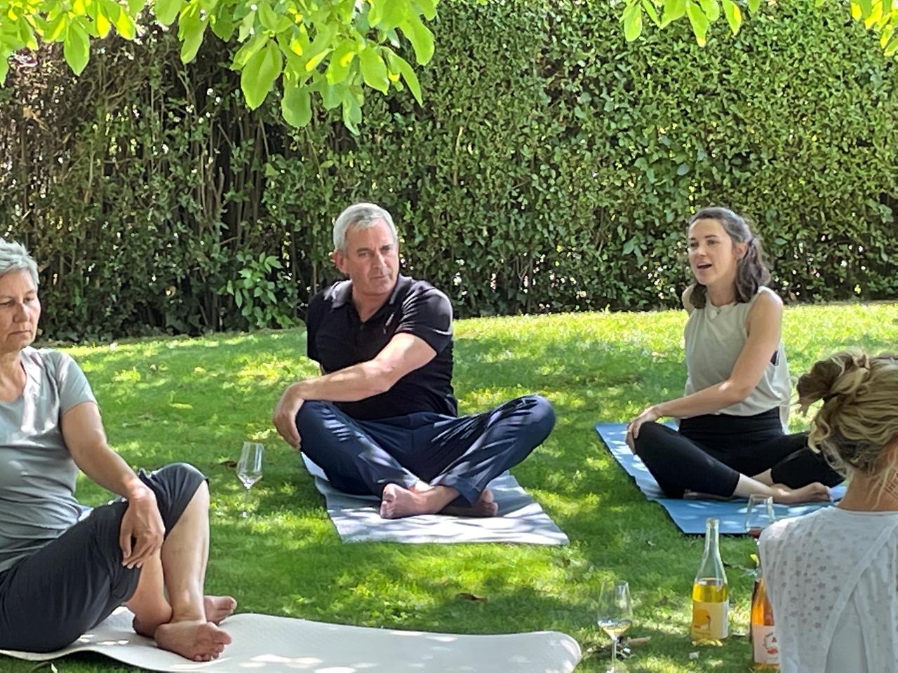Mann auf Yogamatte innerhalb einer Gruppe auf einer Wiese.