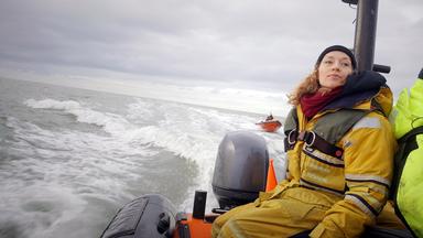 Franziska Saalmann von Greenpeace in gelbem Overall und olivgrüner Schwimmweste fährt im Schlauchboot auf grauer See. Im Hintergrund sieht man ein rotes Boot mit 2 Personen.