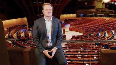 Ein Mann lehnt an einem Geländer im Europarat.