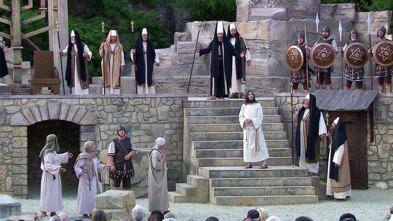 Die Szene zeigt Laienschauspieler in historischen Kostümen, die eine Passionsgeschichte im Römersteinbruch von St. Margarethen darstellen. Die Bühne besteht aus steinernen Strukturen und Stufen.