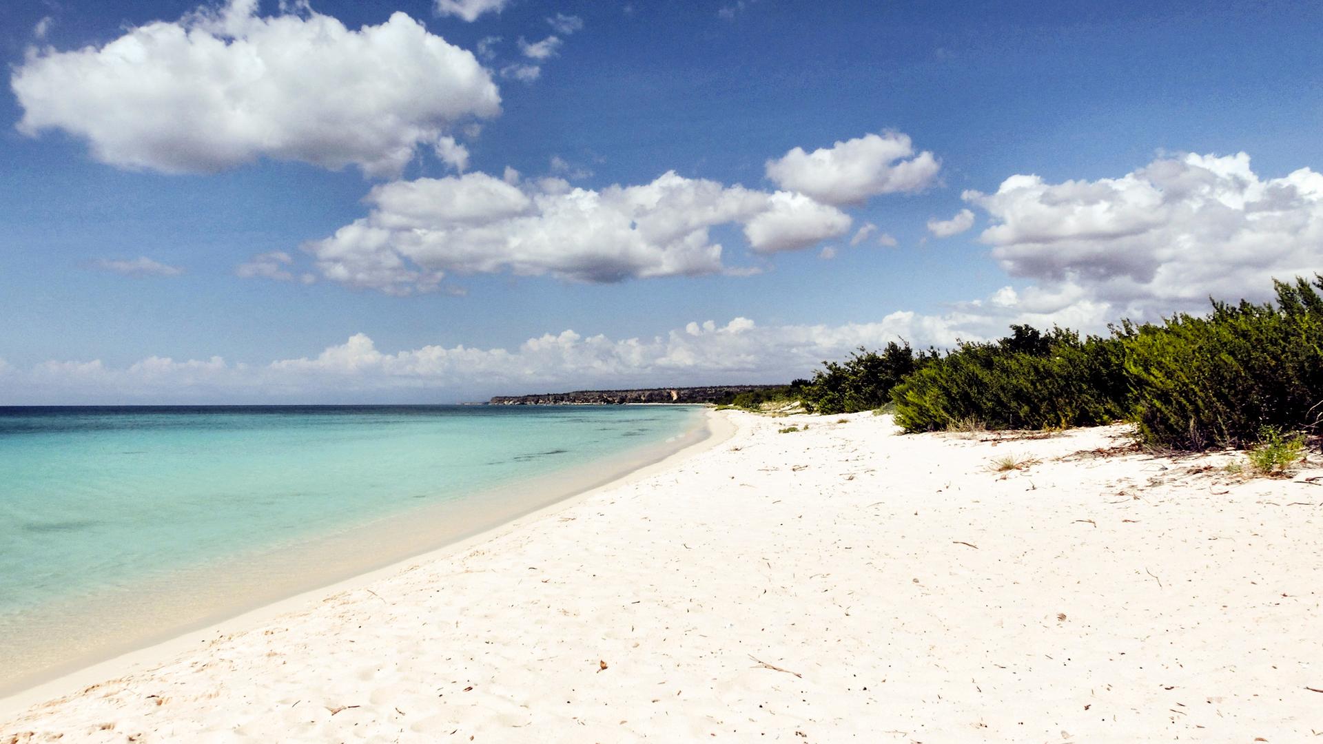 Ein weißer Sandstrand und türkis-blauem Meer und blauem Himmel mit kleinen, weißen Wolken