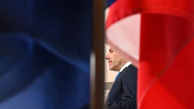 Zwischen österreichischen Flaggen ist ein Mann im Anzug halb verdeckt zu sehen.