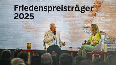 Eine Frau und ein Mann sitzen auf einer Bühne und diskutieren.