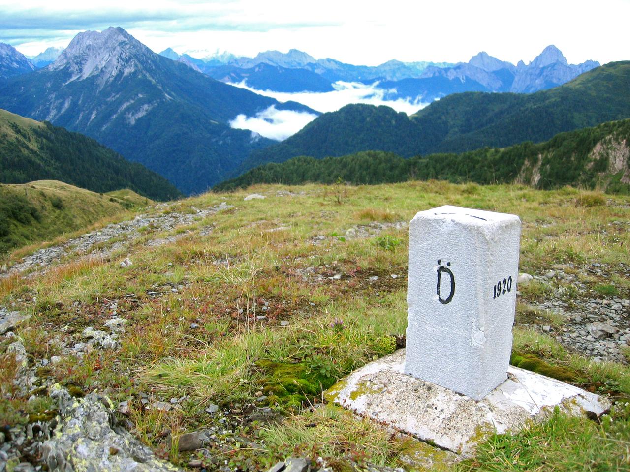 Ein Grenzstein auf einem Berg mit Blick auf Berggipfel