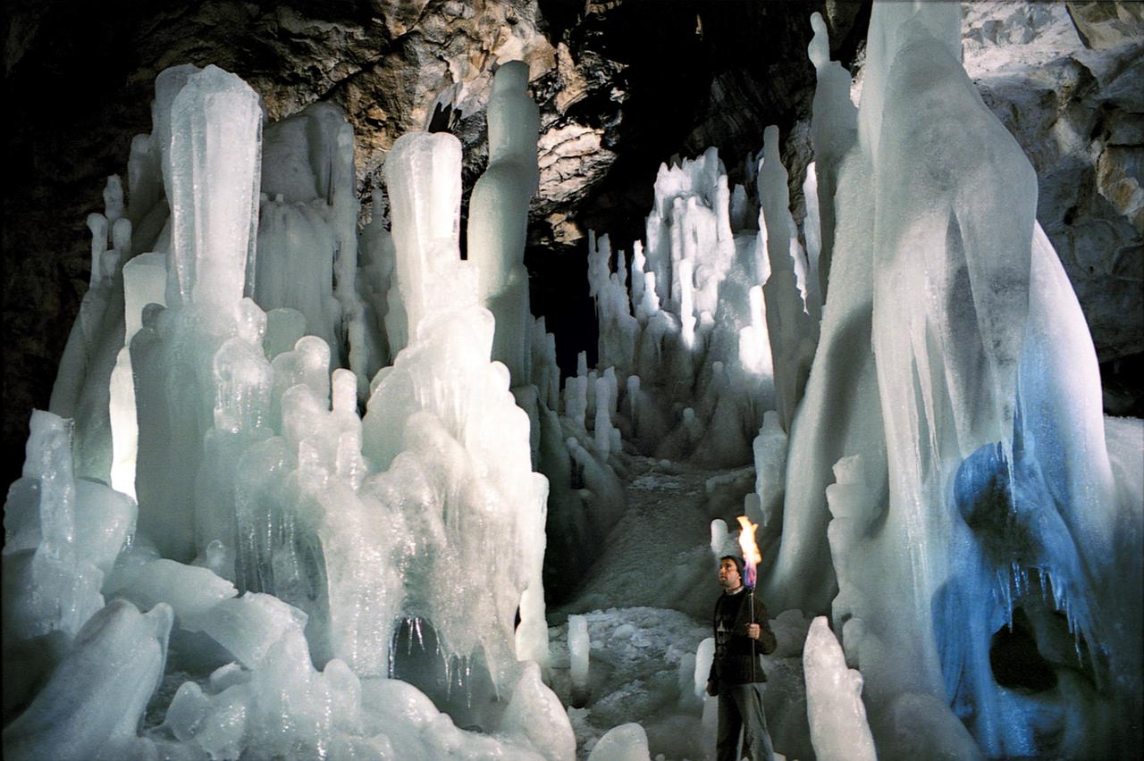Mann mit Fackel zwischen Stalagniten aus Eis.