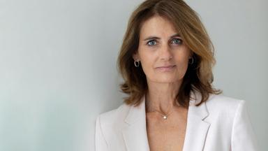 Eine Frau in weißem Blazer schaut in die Kamera.