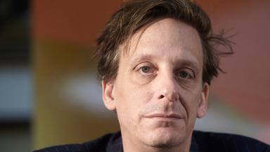 Ein Mann in dunkel gestreiftem Anzug schaut in die Kamera.