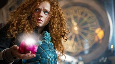 Mädchen mit roten Haaren hält eine leuchtende Blüte in der Hand.