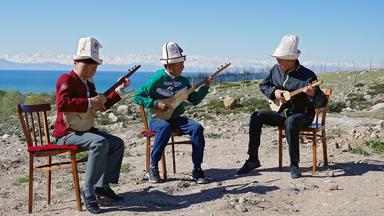 Drei  Jungen sitzen auf einem Berg über dem Meer und musizieren zusammen auf ihren dreisaitigen Gitarren