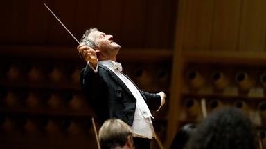 Dirigent Markus Poschner leitet mit ausdrucksvoller Geste ein Orchester während eines Konzerts im modernen Konzertsaal.