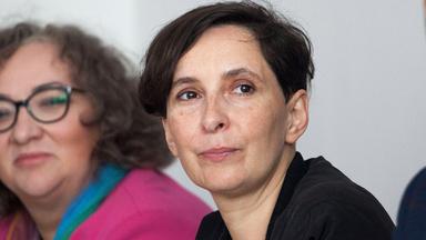 Frau sitzt zwischen zwei Personen u d schaut in die Kamera