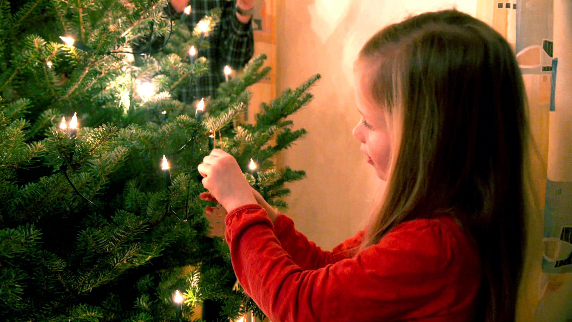 Ein Mädchen hängt ein Lichterkette am Weihnachtsbaum auf.