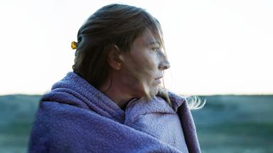 Eine Frau im Profil, sie hat eine lila Wolldecke um sich gewickelt und schaut sorgenvoll