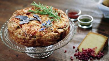 Die Hauptspeise: eine Kartoffel-Lauch-Tarte auf einer schönen Glasform mit lila Blüten garniert.