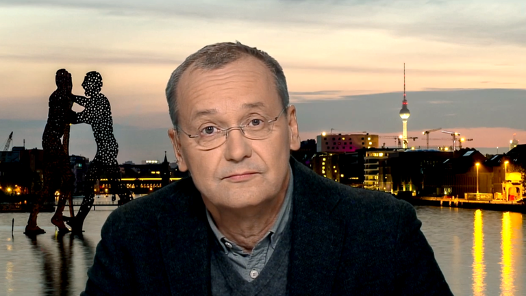 Mann mit Brille vor einer Stadtansicht von Berlin mit dem Alex-Fernsehturm während des Sonnenuntergangs.