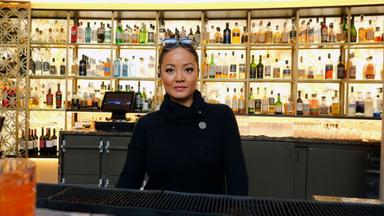 Eine junge Frau hinter dem Tresen einer Bar.