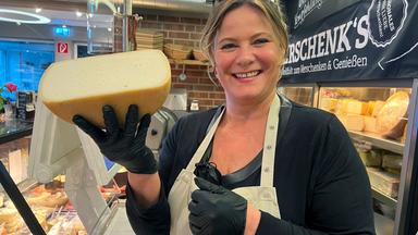 Eine Frau hält Käse in die Kamera.