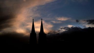 Die zwei Türme des Kölner Doms sind dunkel gegen den Himmel in der Abenddämmerung zu sehen.