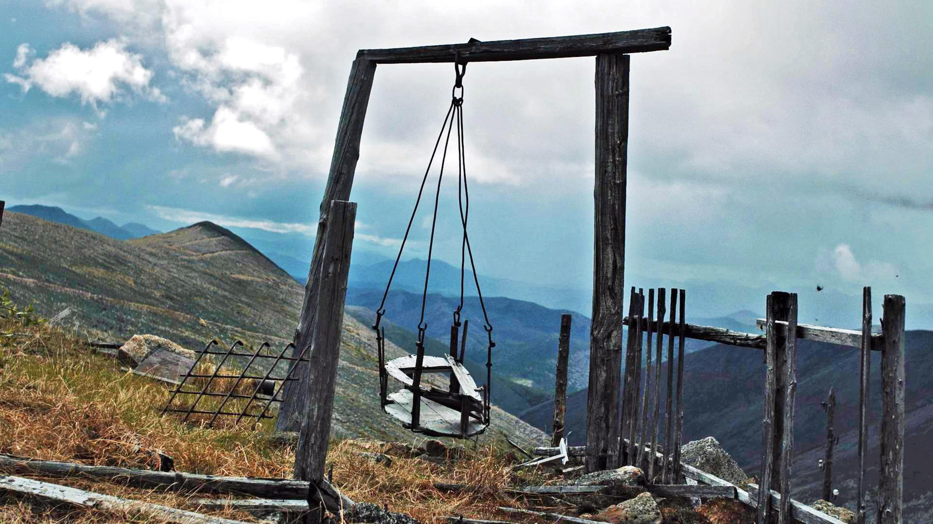 Eine grob gebaute, verwitterte, graubraune leere Kinderschaukel